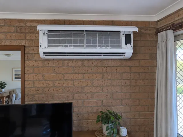 Clean wall-mounted split system with open front panel and visible filters on a brick wall in Blakeview