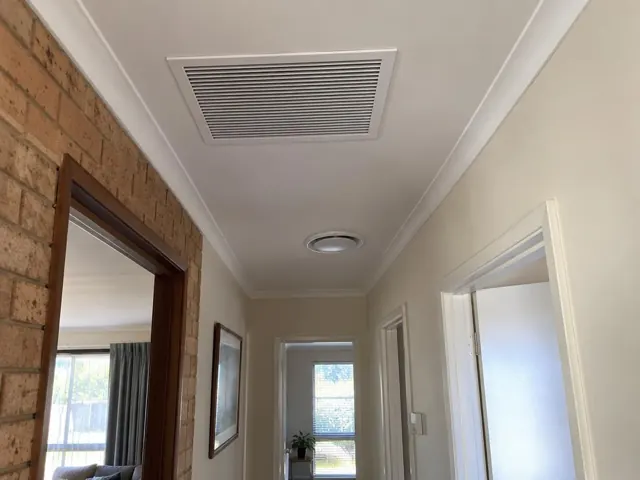 Ceiling return-air grille in a hallway with beige walls and brick feature wall in Hillbank