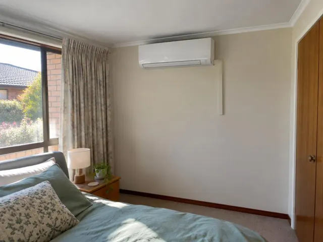 Wall-mounted split system above a bed in a beige bedroom with curtains and timber doors in Salisbury Park